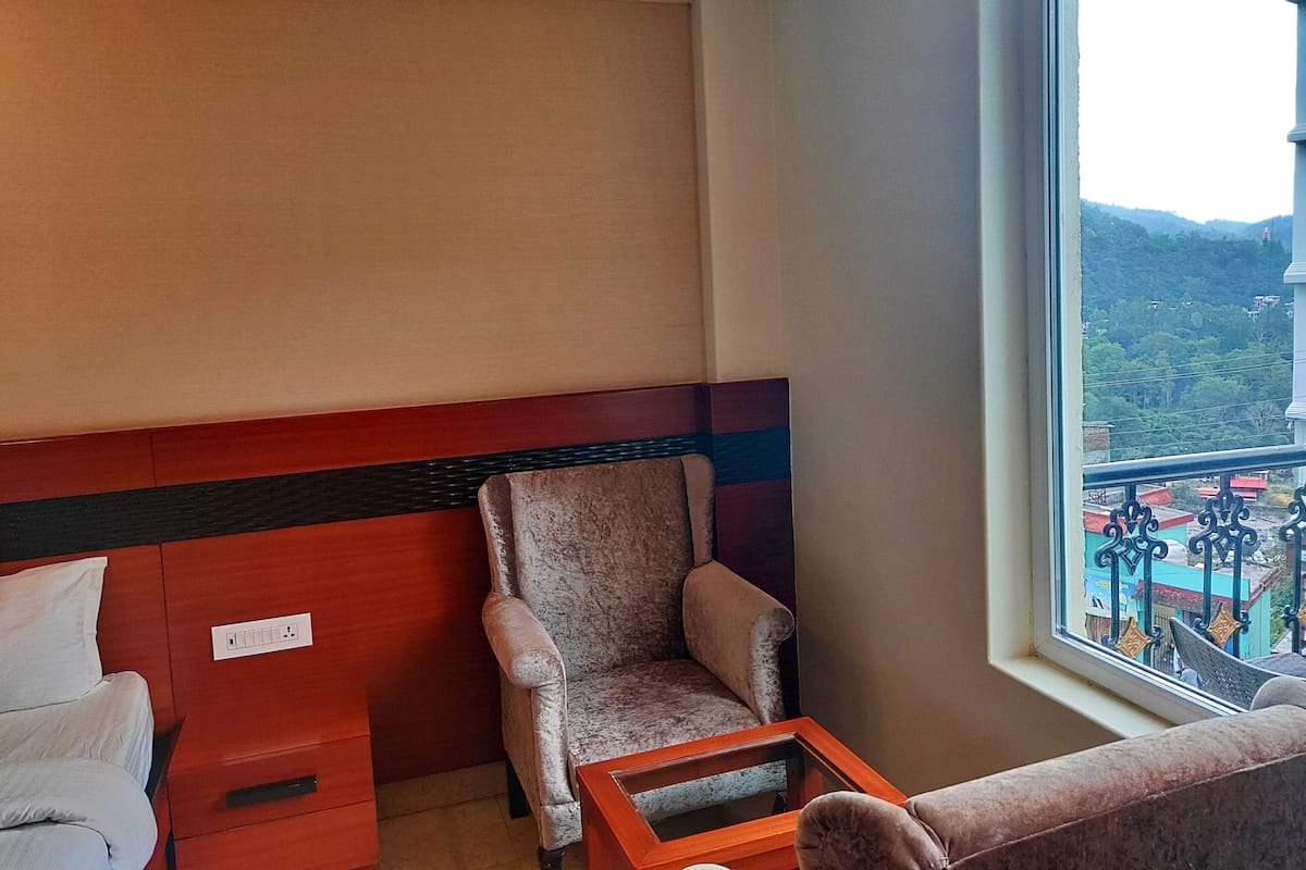 Ein Hotelzimmer mit roter und beiger Wand, einem gepolsterten Sessel, einem kleinen Holztisch und einem Fenster mit Blick auf eine gebirgige Landschaft.