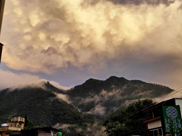 A mountain with clouds in the background and a building with a sign that reads "HOLY RIVER HOTEL". - Holy River Hotel (Narendranagar)