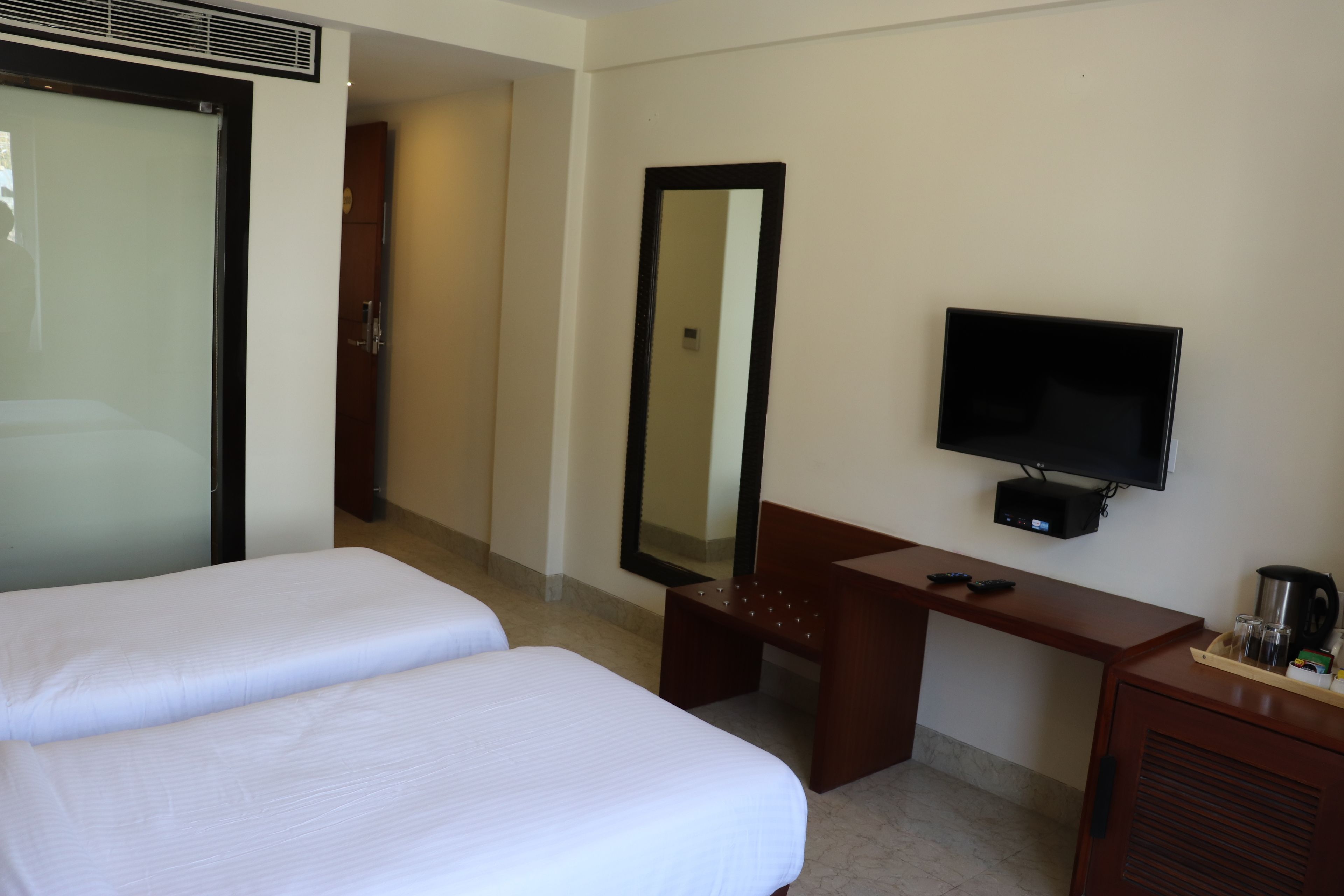 A hotel room with two beds, a desk with a TV, a mirror, and a coffee maker.