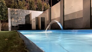 Una piscina con fuente, rodeada por un edificio moderno de fachada de piedra y techo plano.