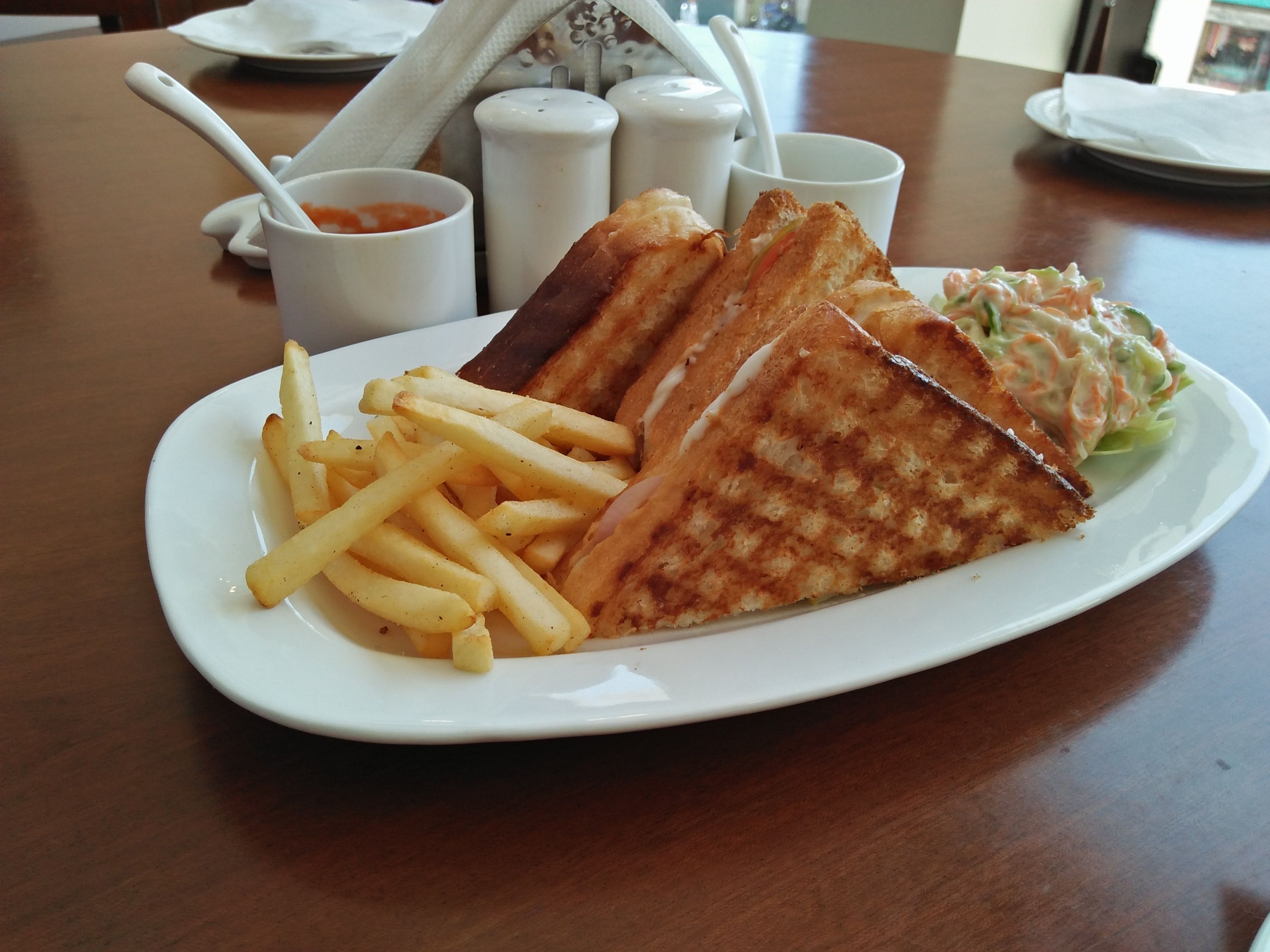 En tallrik med en grillad ostmacka, pommes frites och coleslaw på ett träbord.