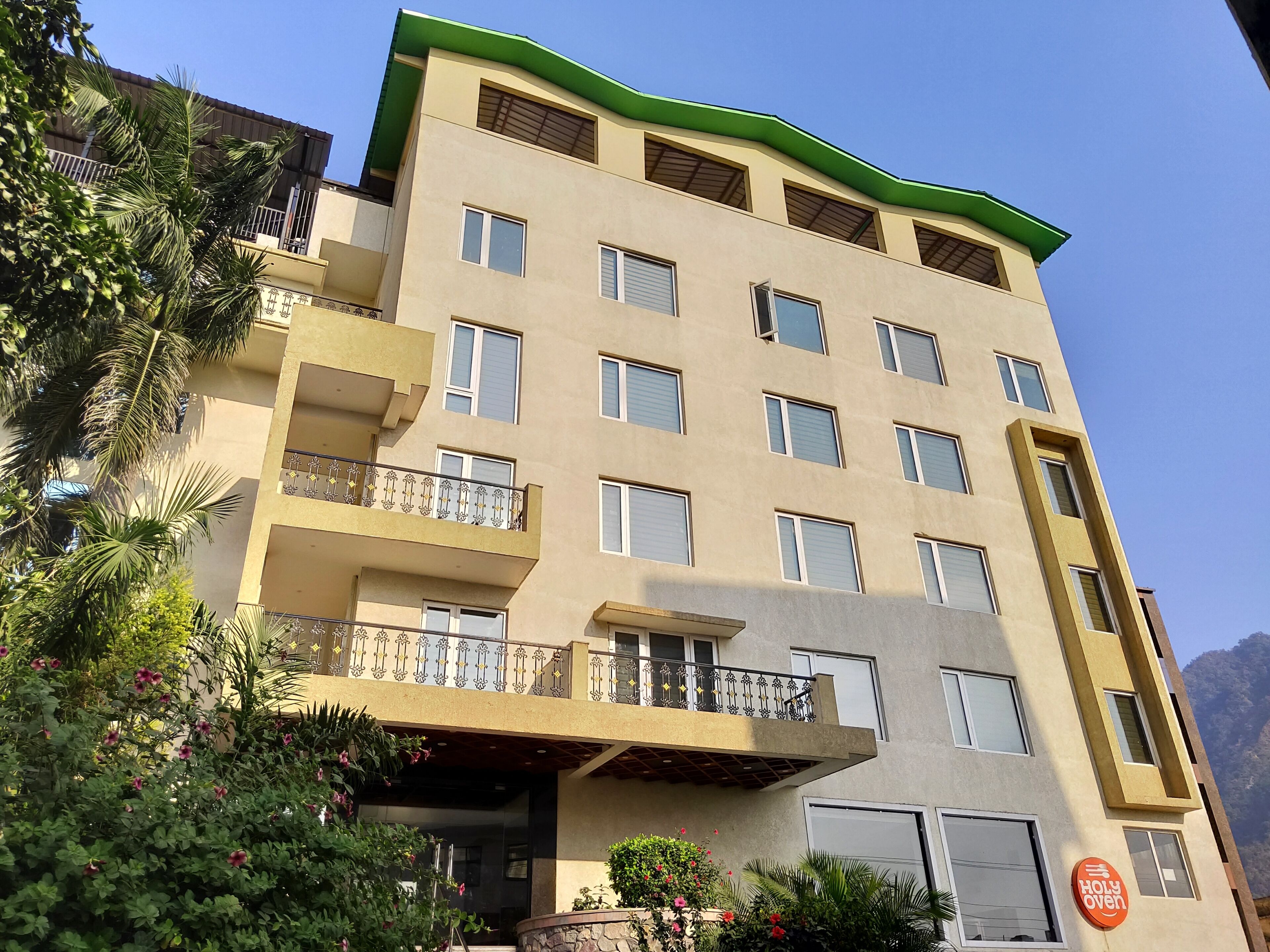 A multi-story building with balconies, a green roof, and a sign for "Holy Oven."
