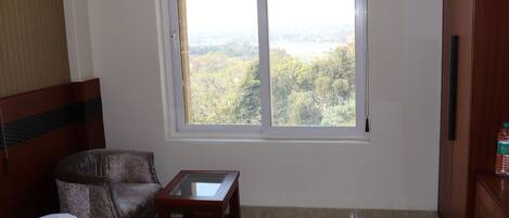 Habitación de hotel con cama, una silla, una mesita y ventana con vista a un área boscosa.