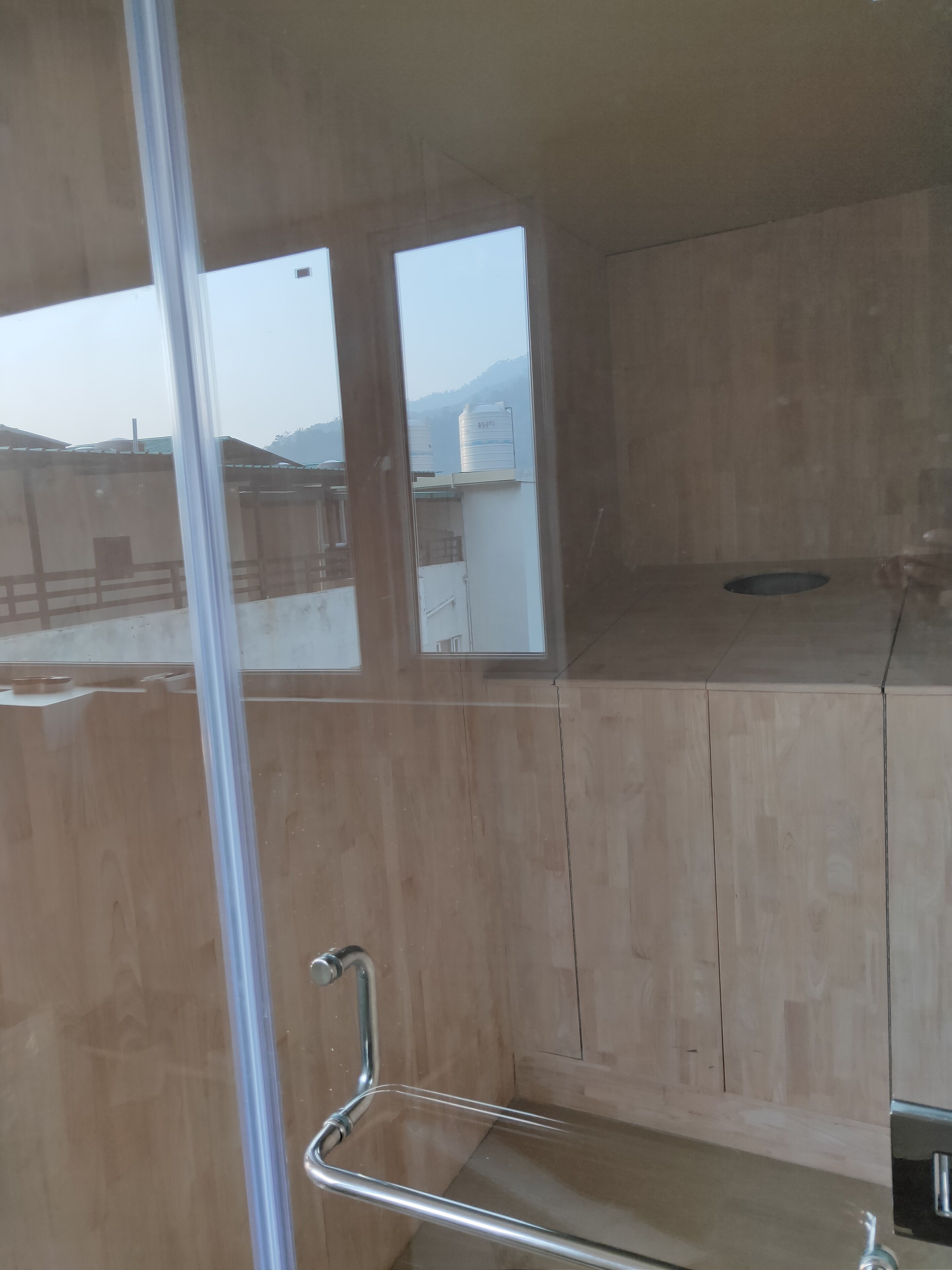 A modern kitchen with wooden cabinets, a stainless steel sink, and a window overlooking a building and mountains.