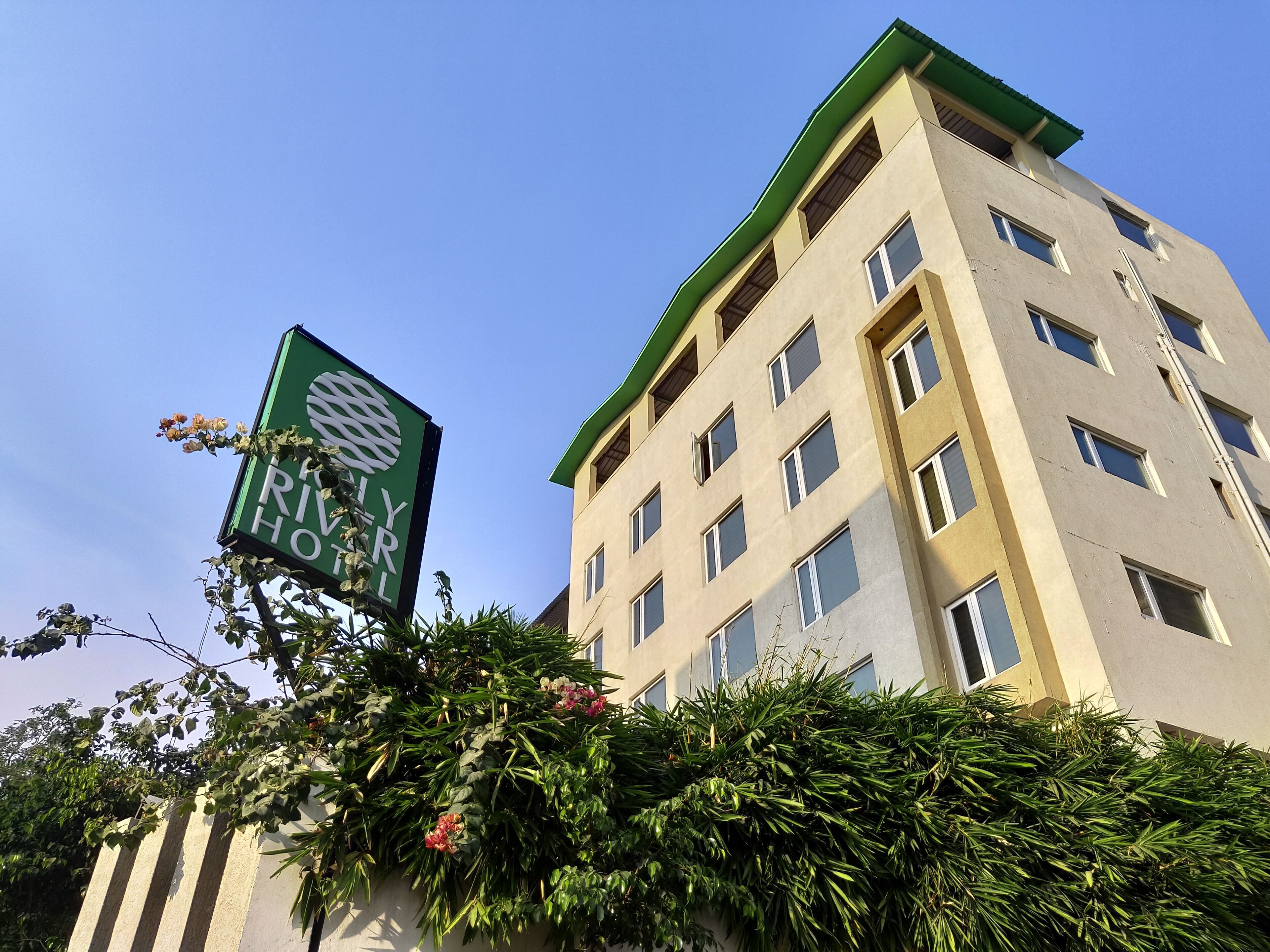 A multi-story hotel with a green signboard, surrounded by lush greenery.