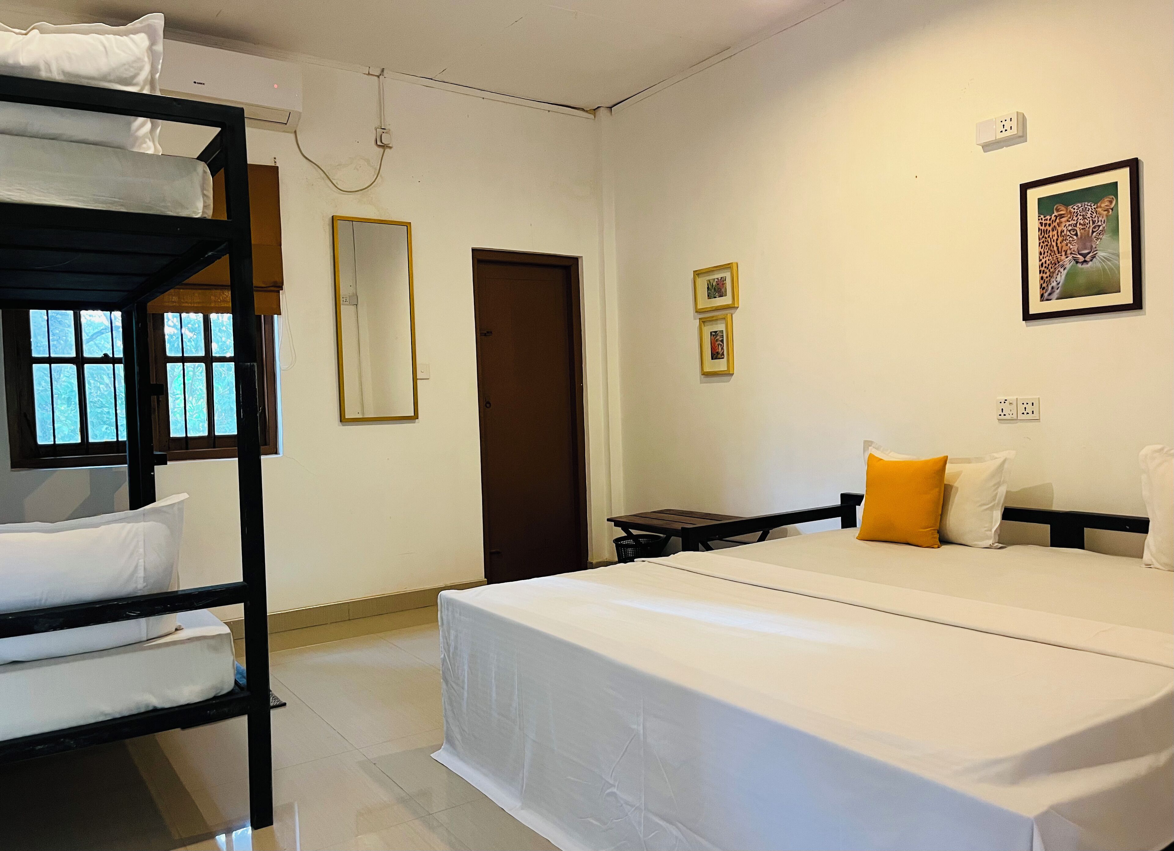 Habitación de hotel con literas, una cama individual, una mesita pequeña, una silla, un espejo, una puerta y un cuadro en la pared.