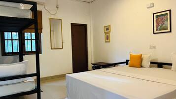 Habitación de hotel con literas, una cama individual, una mesita pequeña, una silla, un espejo, una puerta y un cuadro en la pared.