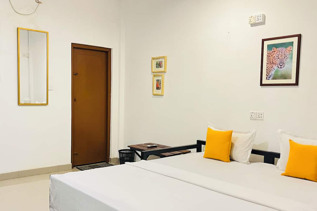 Quarto de hotel com cama, escrivaninha, cadeira, porta e parede com espelho e quadros.