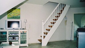 Un salon avec un escalier, un téléviseur et un meuble avec des portes en verre.