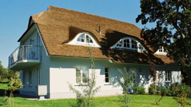 Une maison à deux étages avec un toit de chaume, un balcon au premier étage et une pelouse bien entretenue.
