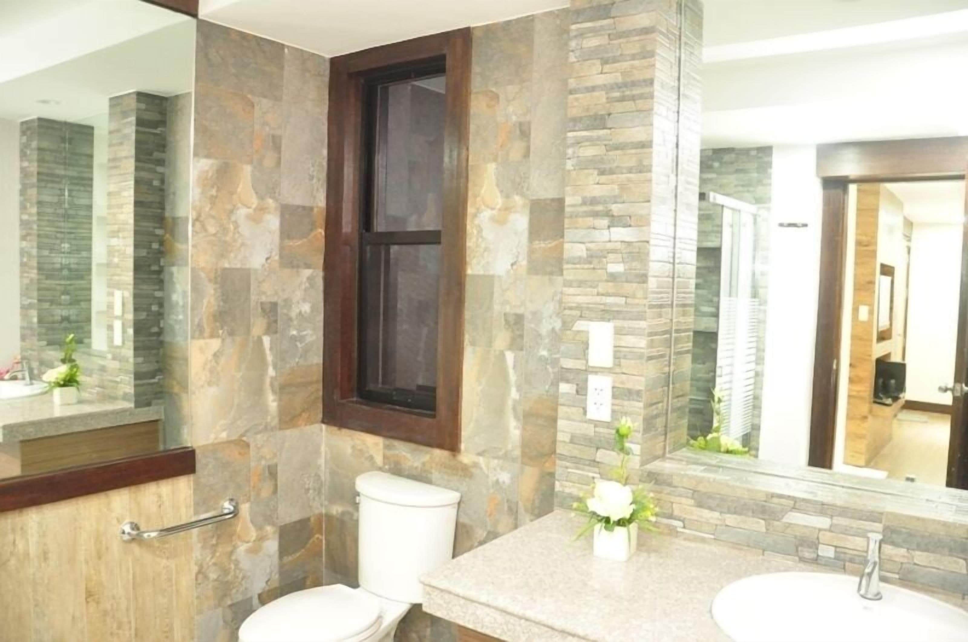 A bathroom with a stone wall, a window, a toilet, and a sink with a mirror.