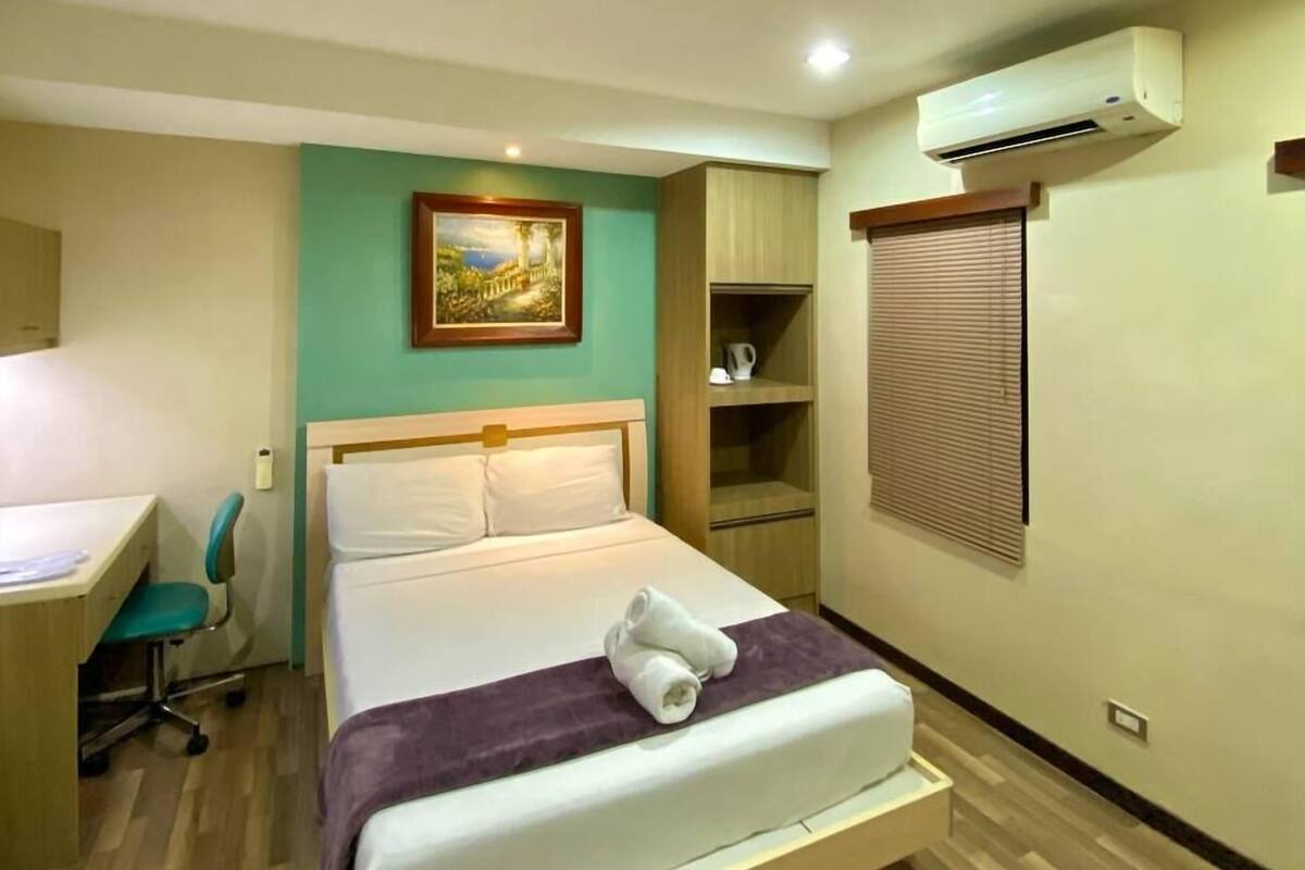 Ein Hotelzimmer mit Bett, Schreibtisch, Stuhl, Klimaanlage und einem Bild an der Wand.
