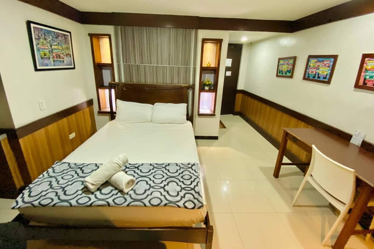 Ein Hotelzimmer mit Bett, Schreibtisch und Stuhl. An den Wänden befinden sich Bilder in Rahmen.