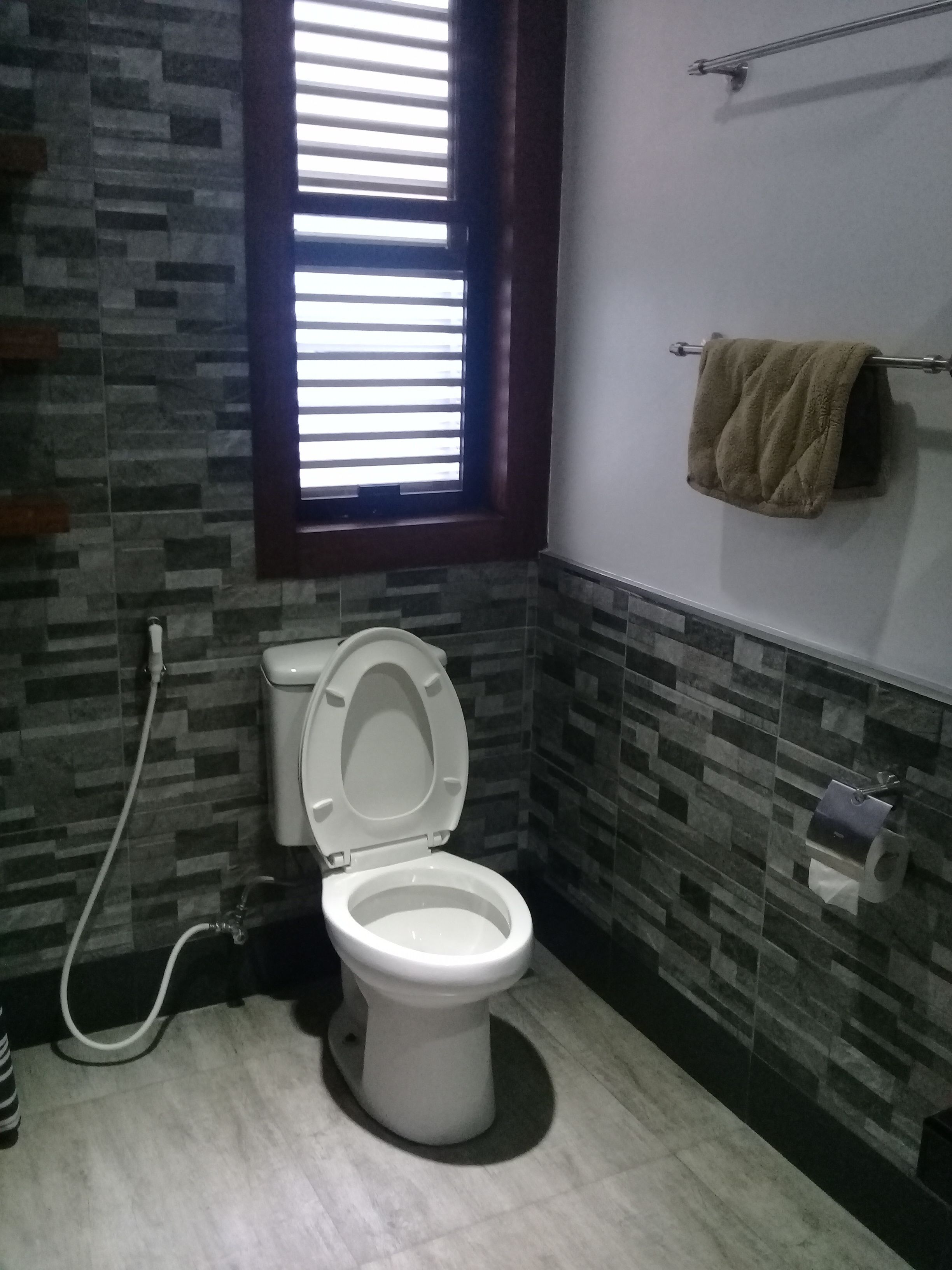 A bathroom with a toilet, a towel rack, and a window with blinds.