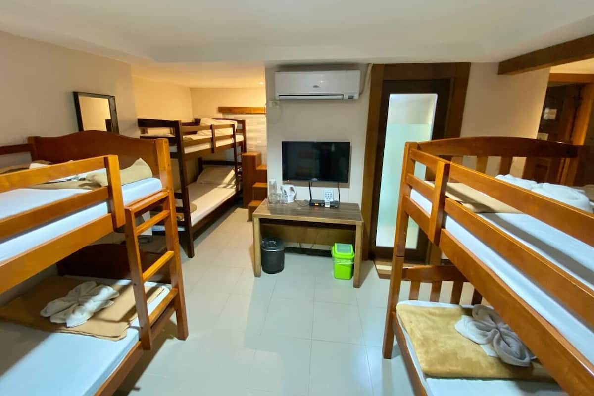 Ein Schlafsaalzimmer mit Etagenbetten, einem Fernseher, einem kleinen Tisch und einem Mülleimer.