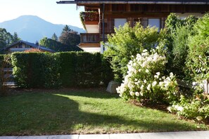 Una casa de madera con balcón, rodeada de abundante vegetación y una montaña al fondo.