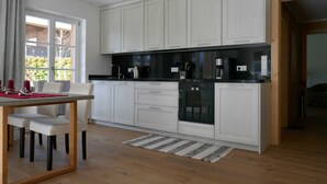 A modern kitchen with white cabinetry, a black countertop, and a dining area with a table and chairs. - Bodenschneid Suite Garden View West - Bodenschneid Suites Rottach-Egern (Rottach-Egern)