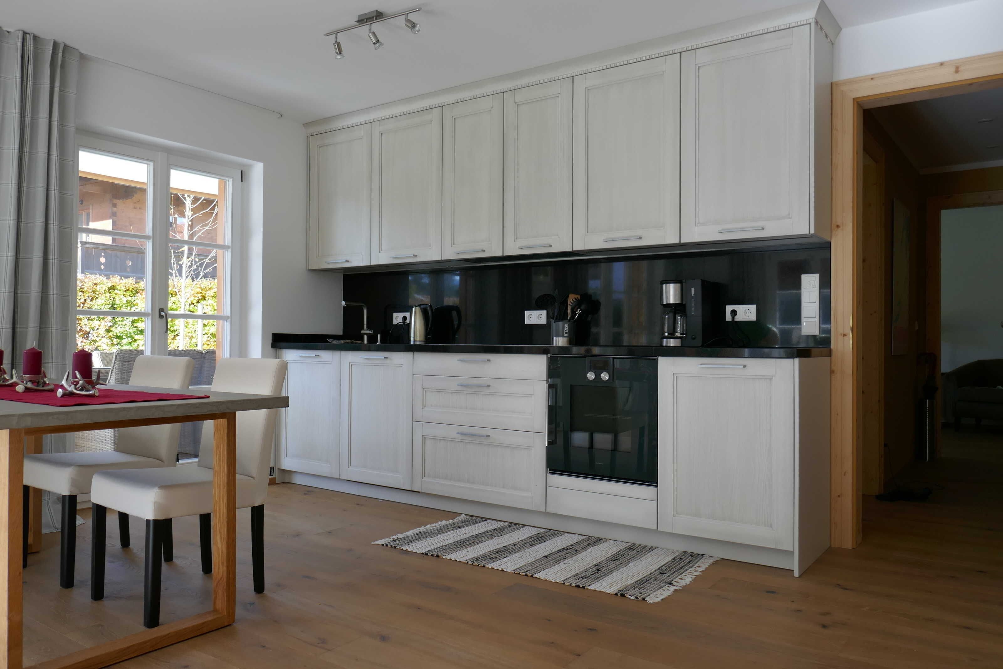 A modern kitchen with white cabinetry, a black countertop, and a dining area with a table and chairs.