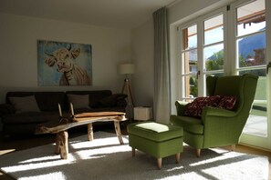 Una sala de estar con una mesa de centro de madera, un sillón verde, un sofá y un cuadro en la pared.