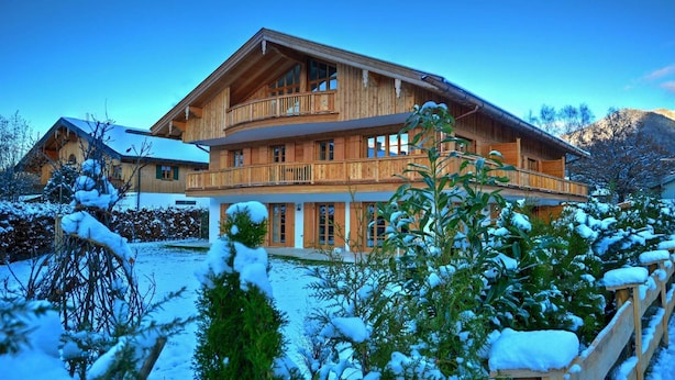 A large wooden chalet with multiple balconies, surrounded by snow-covered trees and mountains. - Bodenschneid Suite Garden View West - Bodenschneid Suites Rottach-Egern (Rottach-Egern)
