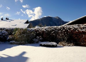 A snow-covered landscape with a mountain in the background, a hedge, and a building with a sloped roof. - Bodenschneid Suite Garden View West - Bodenschneid Suites Rottach-Egern (Rottach-Egern)