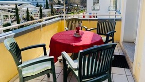Ein Balkon mit einem roten Tisch, vier Stühlen, einem gelben Sonnenschirm und Blick auf Gebäude und Bäume.