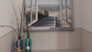 A room with a large window overlooking a beach. There are two vases with decorative items on a shelf below the window.