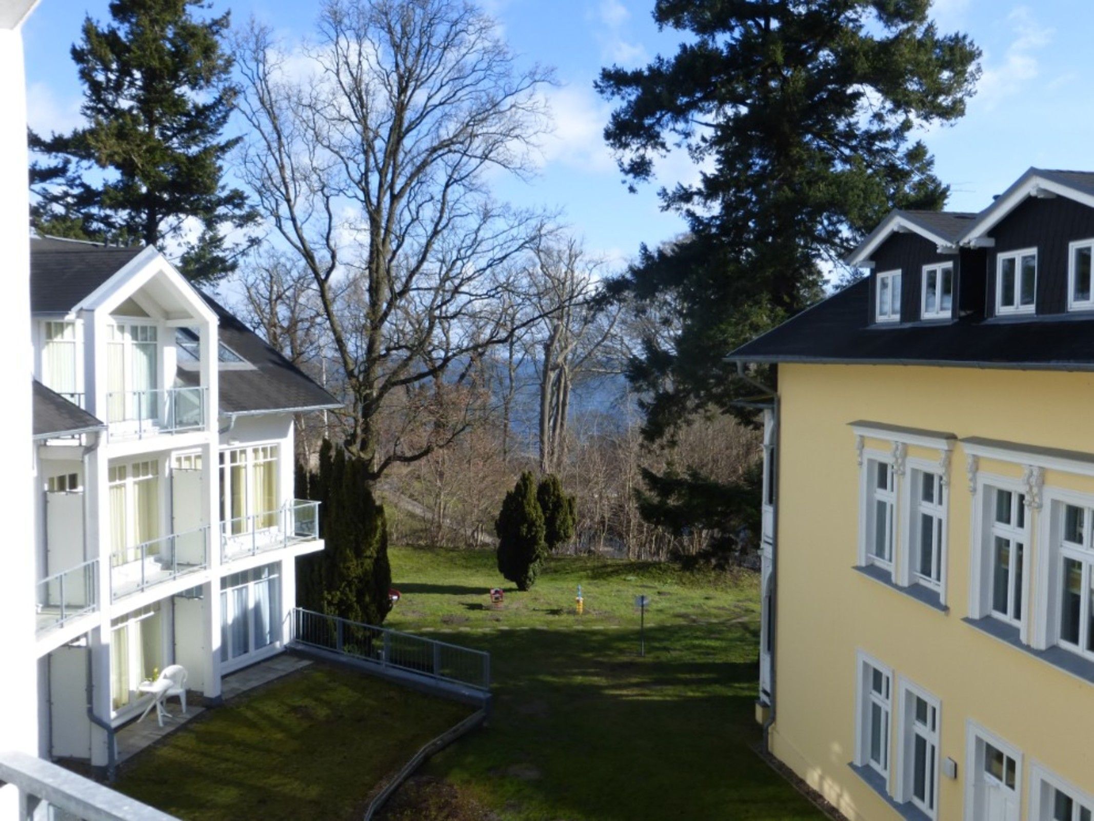 Ein zweistöckiges Gebäude mit einem Balkon im oberen Geschoss, einem gepflegten Rasen und einem großen Baum im Hintergrund.
