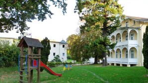 A playground with a slide and climbing structure, surrounded by a grassy area and trees.