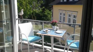 Ein Balkon mit Tisch und Stühlen für zwei Personen, ein Vogel auf dem Geländer und ein gelbes Gebäude im Hintergrund.