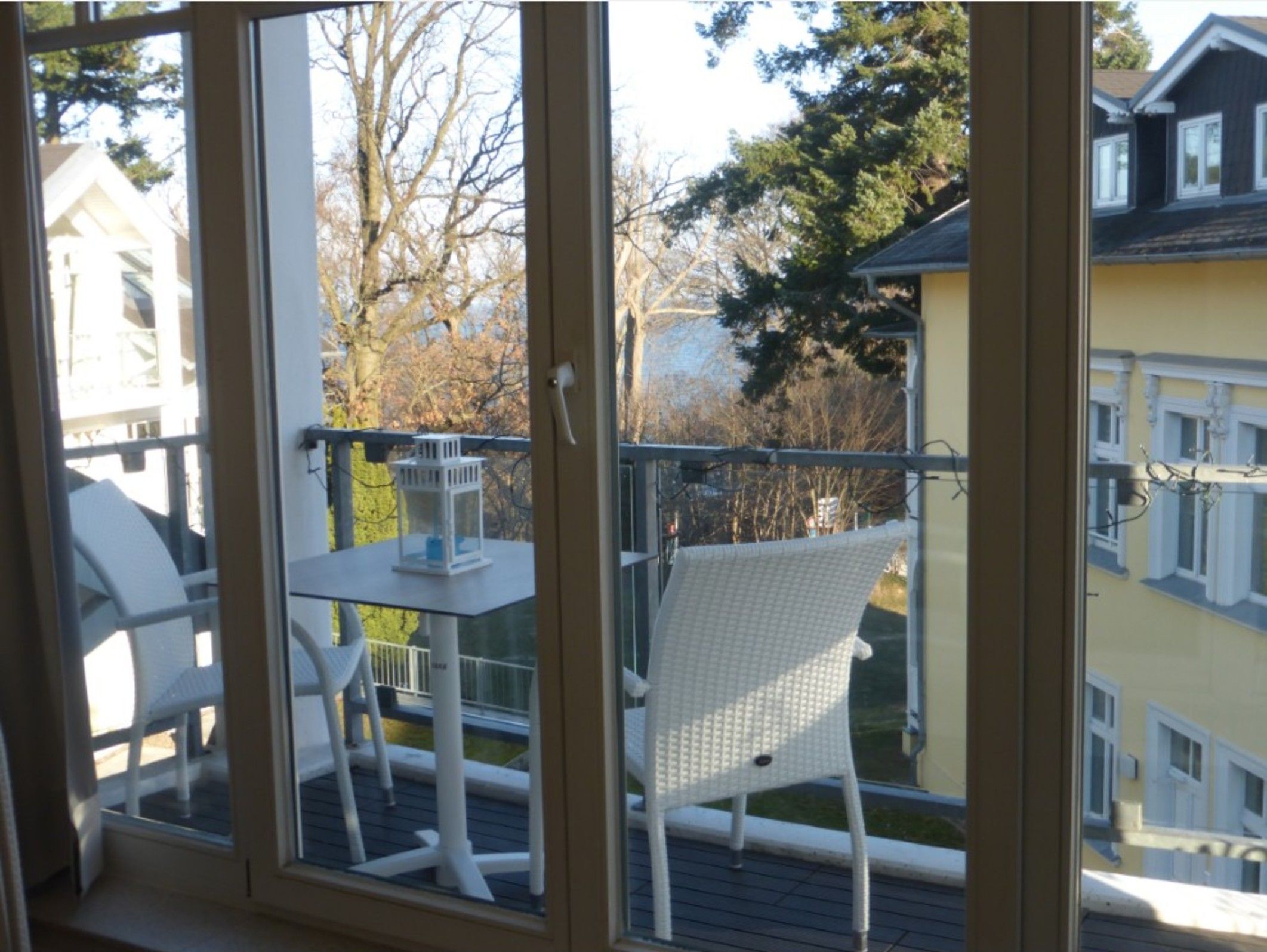 Ein Balkon mit weißem Stuhl und kleinem Tisch, mit Blick auf ein Wohngebiet mit Bäumen und Häusern.