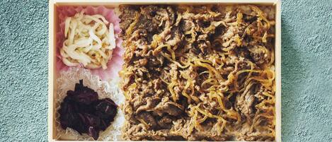 Una caja rectangular con carne desmenuzada, cebollas encurtidas y una porción pequeña de col.