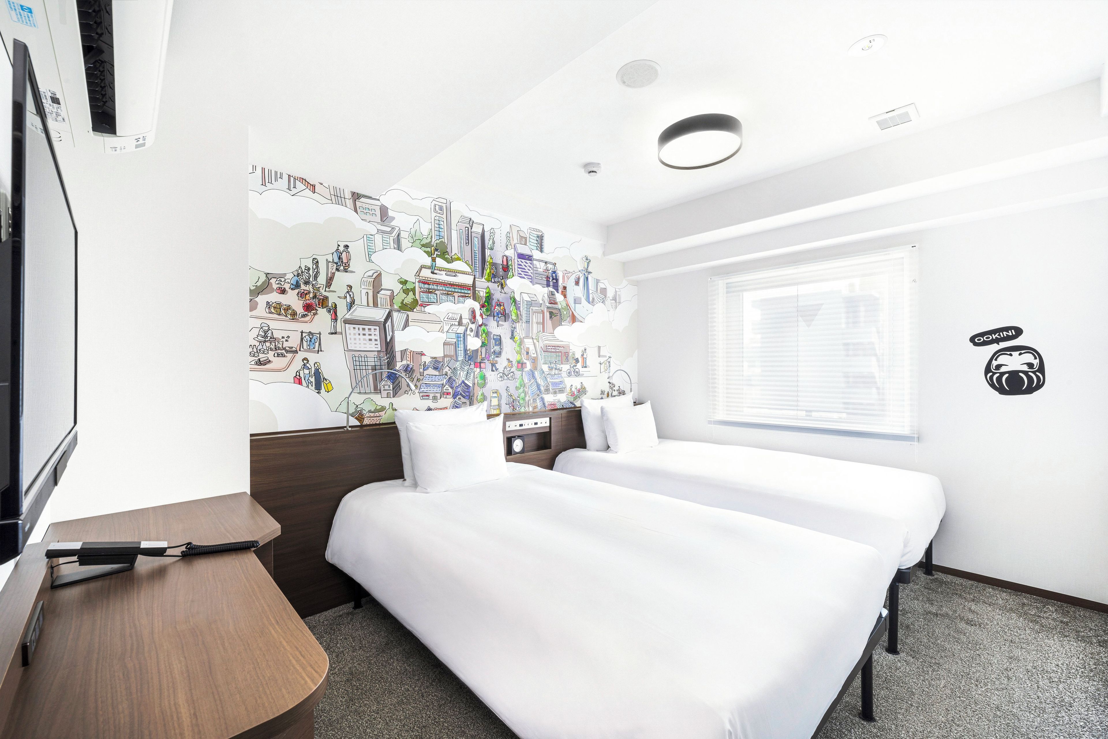 Une chambre d’hôtel avec un lit, une table de chevet et un mur orné d’une fresque représentant un paysage urbain.