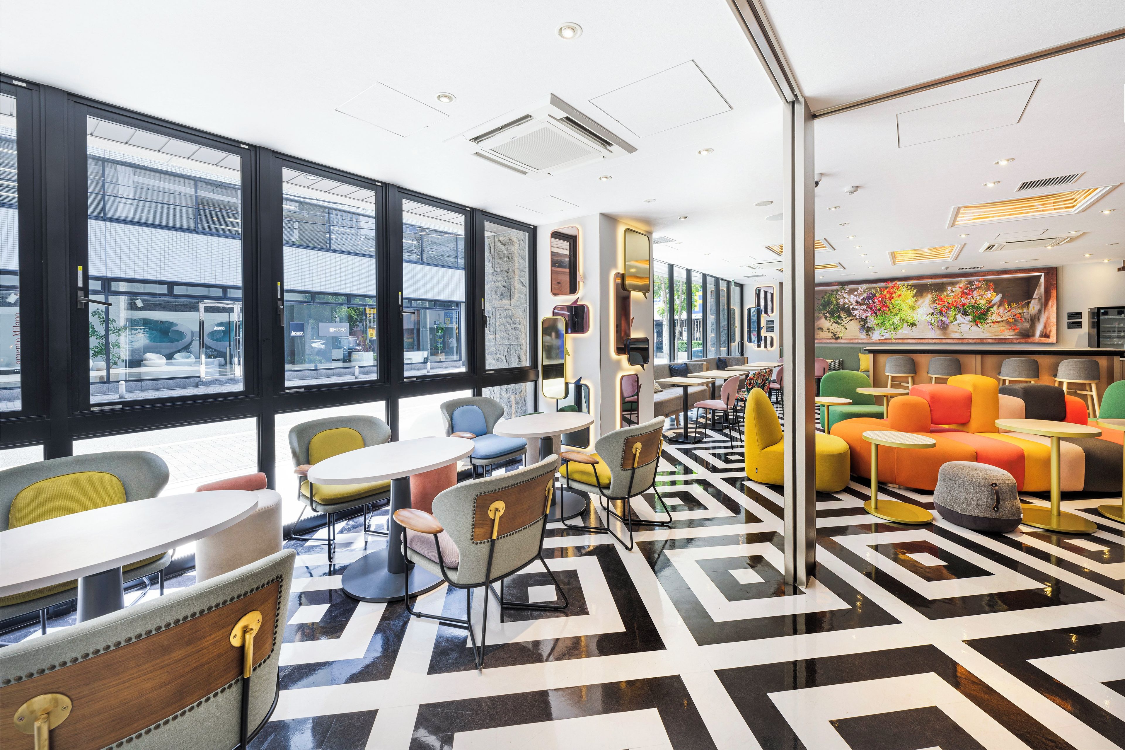 A modern interior with large windows, a geometric patterned floor, and colorful seating areas.