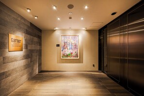 Pasillo de hotel con un ascensor moderno, una obra de arte enmarcada en la pared y un cartel que indica la ubicación del hotel.