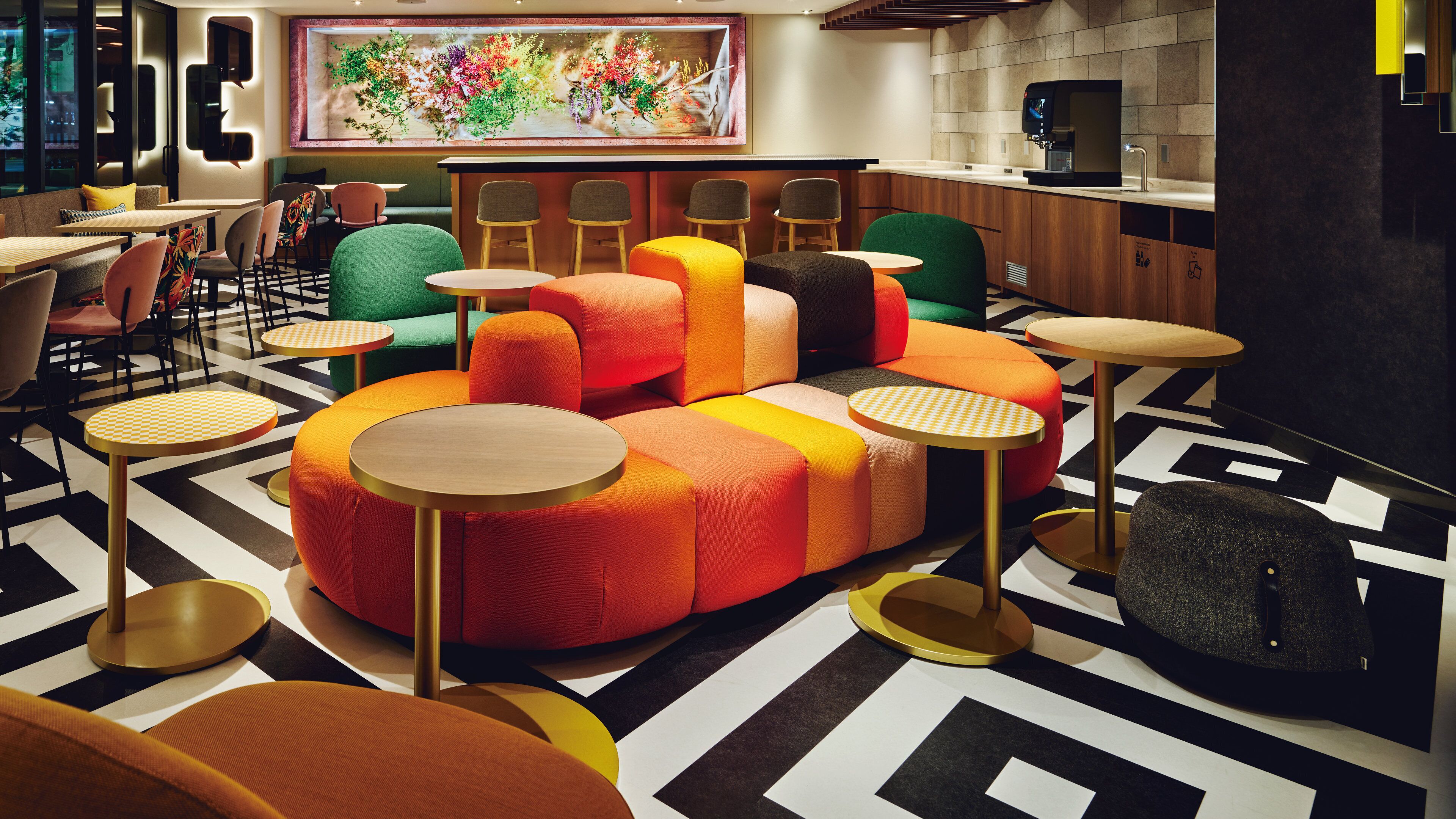 A modern lounge area with colorful seating, small round tables, and a large abstract painting on the wall.
