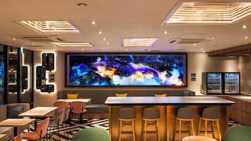 A modern bar area with a large digital screen, seating arrangements, and a patterned floor.