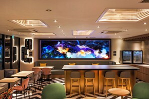 Un área de bar moderna con una gran pantalla digital, arreglos de asientos y un piso con diseño.