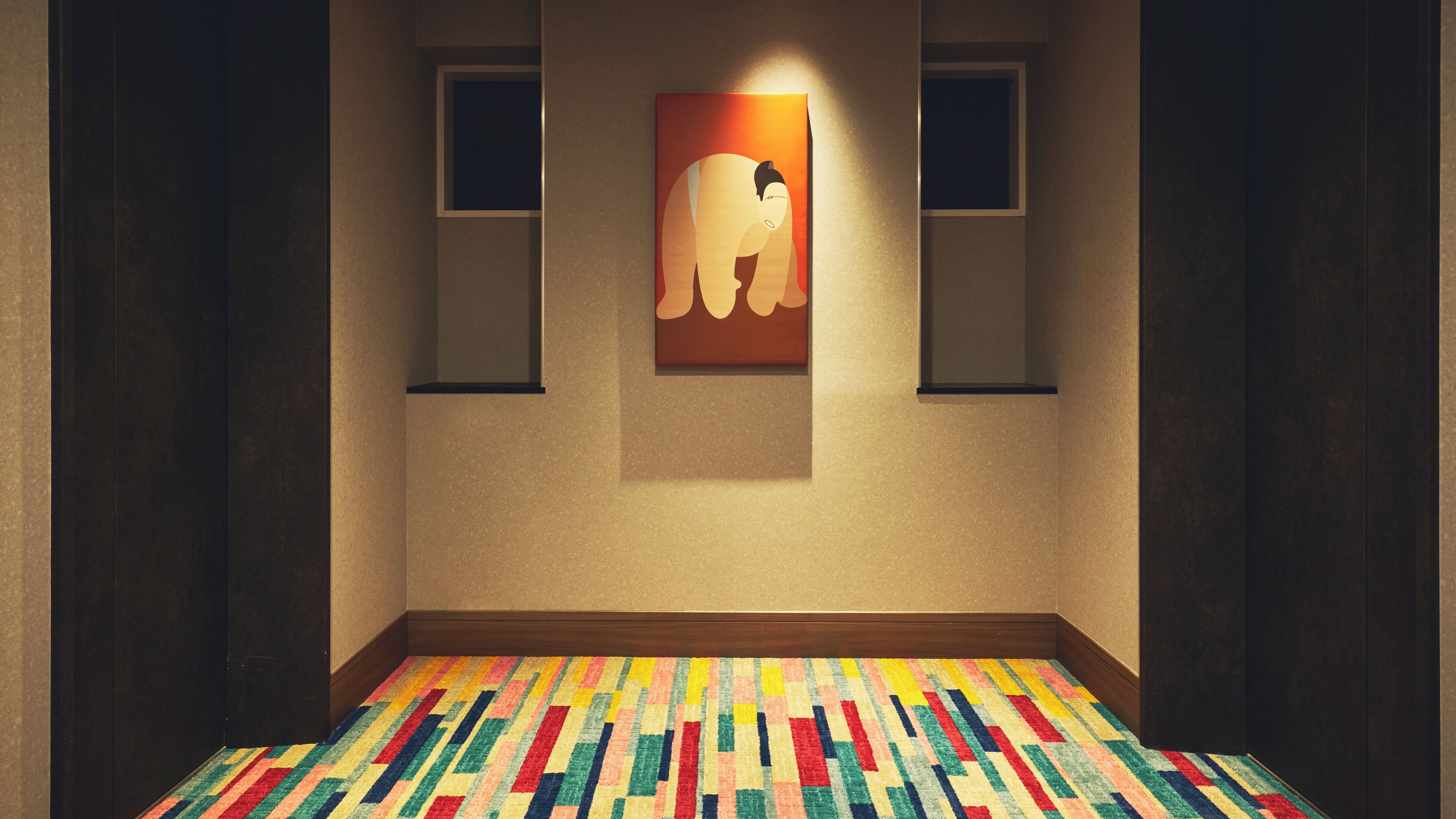 A hallway with a colorful patterned carpet, a framed artwork of an elephant, and two small windows.