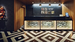 Zona de recepción de un hotel con diseño moderno, que incluye un mostrador de recepción, cuadros enmarcados en la pared y un piso con estampado.
