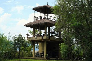 A multi-level wooden structure with thatched roofs, surrounded by lush greenery.