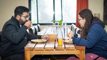 Two people sitting at a wooden table with a plant, a glass of orange juice, and a bottle of water.