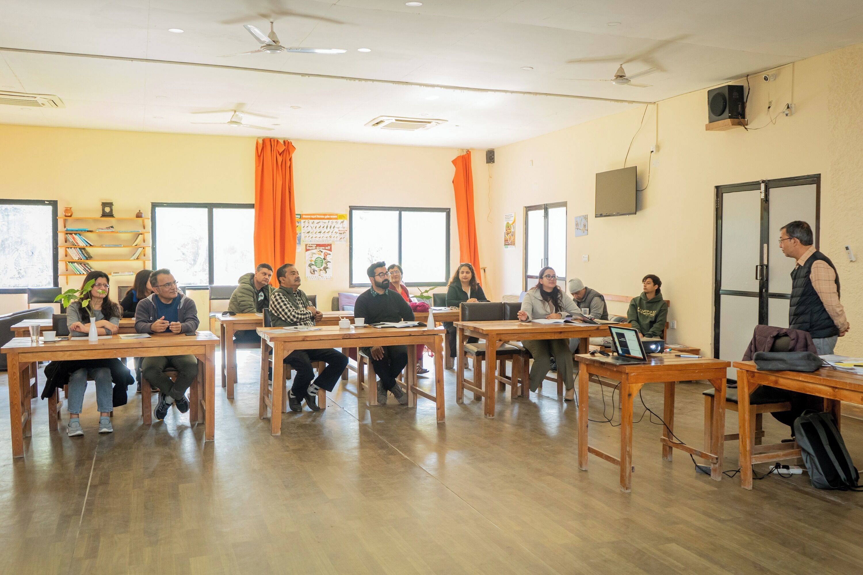 A classroom with wooden desks and chairs, a whiteboard, and a projector screen.