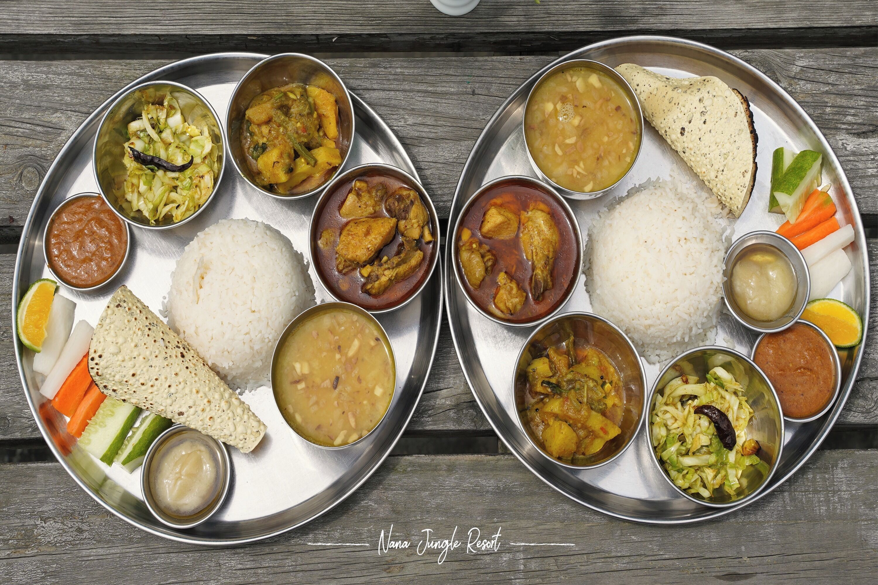 Two metal plates with various dishes including rice, curries, and vegetables.