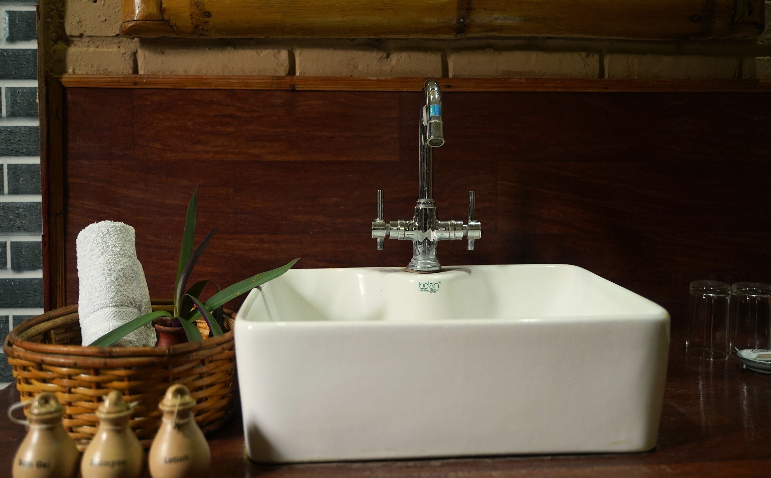 Un lavabo de salle de bain avec un robinet, un bac blanc et un panier contenant une serviette et des flacons de savon.