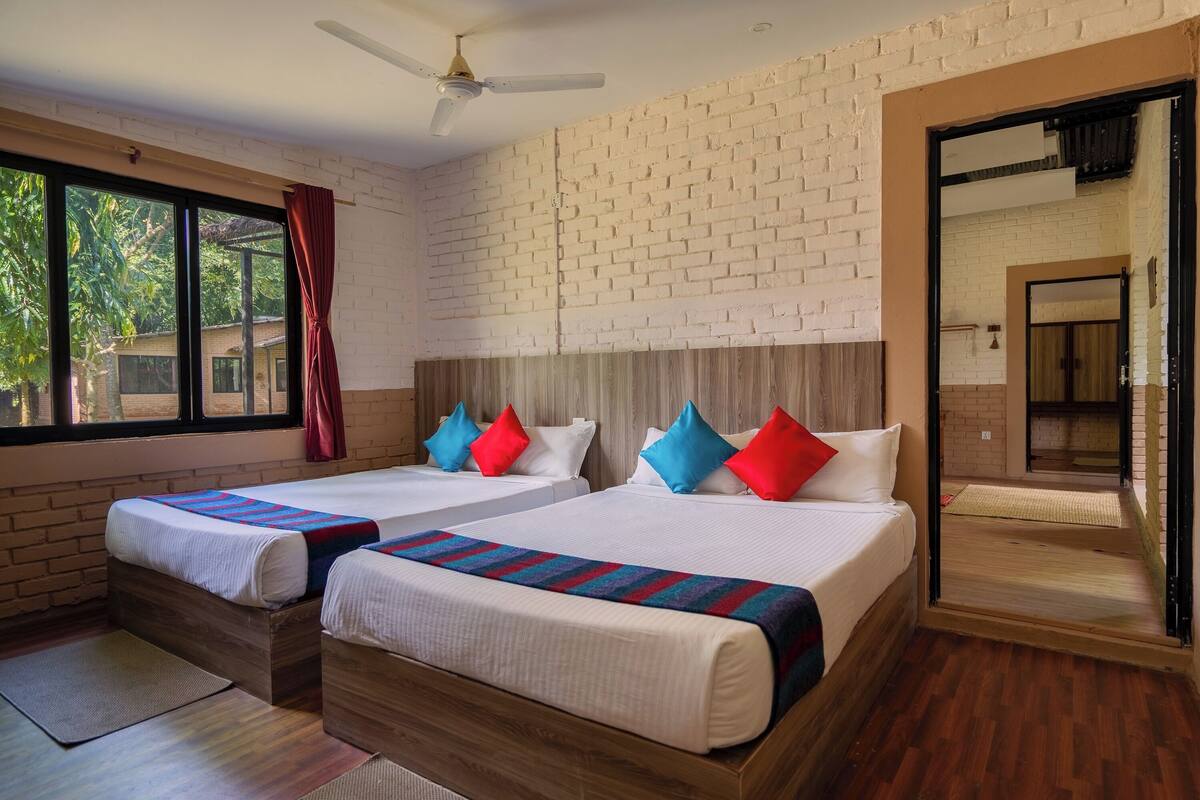 Habitación de hotel con dos camas, cabecero de madera, pared de ladrillo y un ventanal grande.