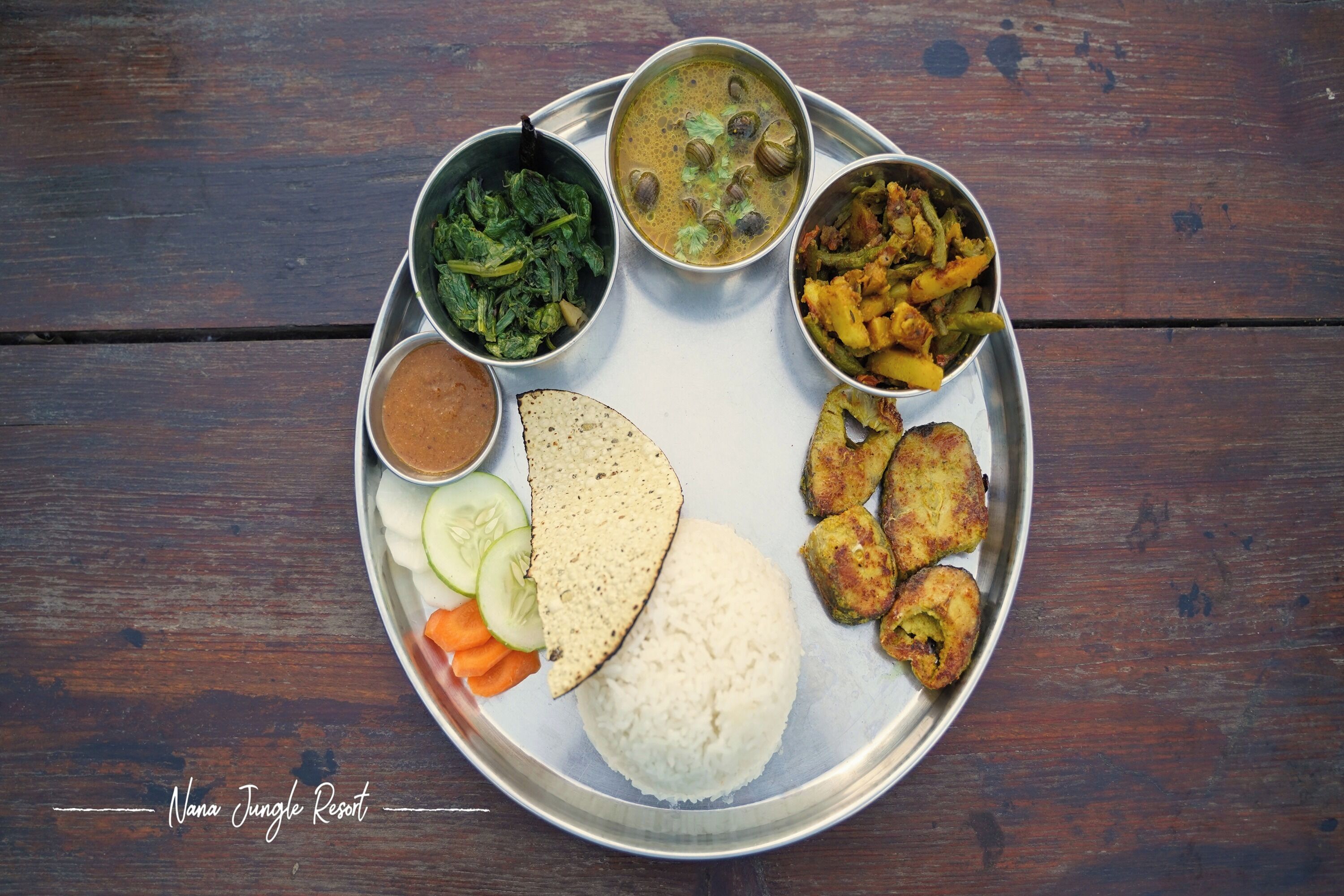 A meal with rice, flatbread, vegetables, and curry on a metal plate.