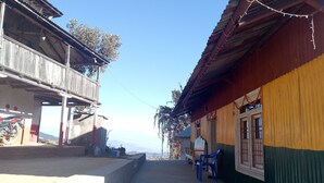A narrow street with buildings on either side, a motorcycle parked on the left, and a blue plastic chair on the right. - Mount Mahabharat Homestay (Dhunkharka)