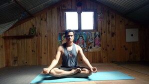 A person meditating on a yoga mat in a room with wooden walls, a slanted ceiling, and a window. - Mount Mahabharat Homestay (Dhunkharka)