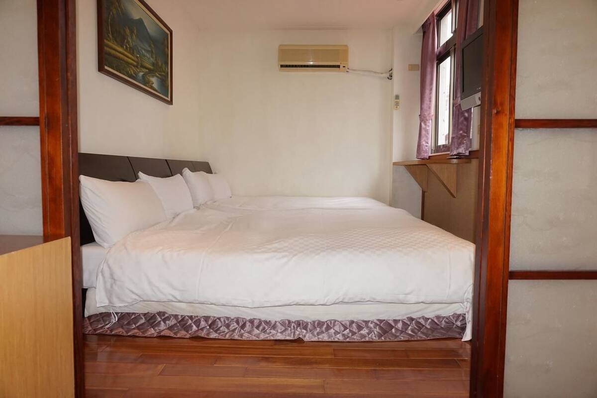 A neatly made bed with a white duvet, a wooden headboard, and a window with curtains.